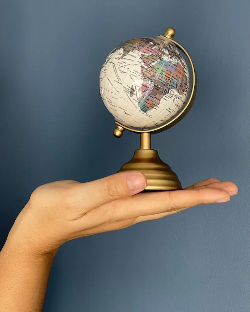 Uma mão segurando um pequeno globo terrestre, simbolizando a conexão global e a interculturalidade.